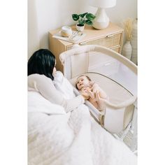 a baby laying in a crib next to a woman with her hand on the infant's head