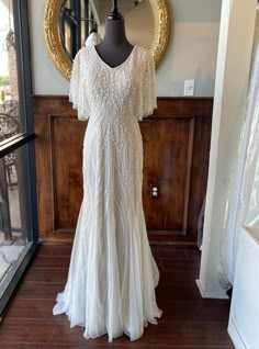 a white dress is on display in front of a mirror with a gold framed mirror behind it