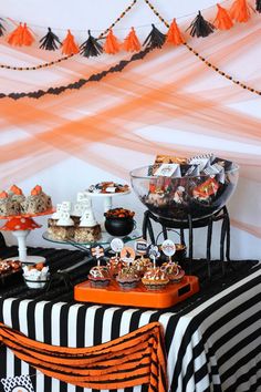 a halloween dessert table with candy and treats on it's tablespread, decorated in orange and black