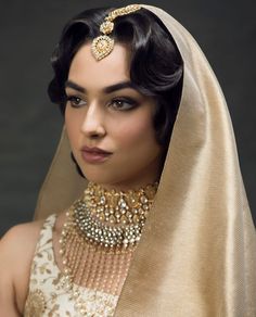 a woman wearing a gold and white dress with a veil over her head is looking at the camera