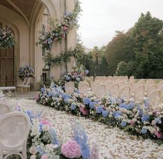 rows of white chairs with blue and pink flowers on the ground in front of an archway