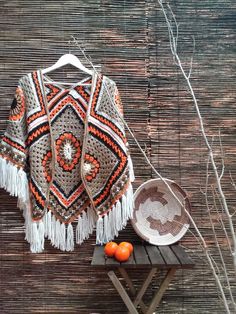 a crocheted shawl sits on a table next to oranges and a basket