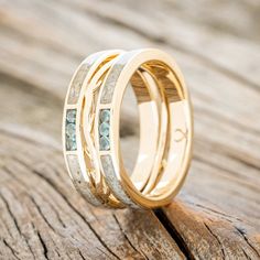 two gold wedding bands with blue diamonds on them sitting on a piece of drift wood