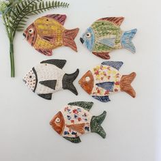 four ceramic fish sitting on top of a white surface next to a plant with green leaves