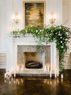 a fireplace with candles and flowers on it in a room that is decorated with white walls