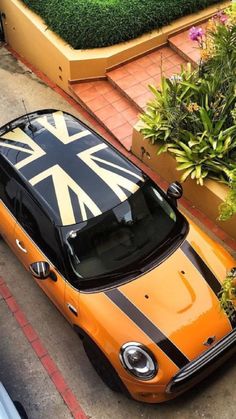 an orange and black mini car parked on the side of the road next to some plants