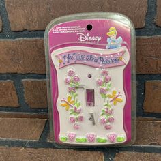 a pink and white light switch cover with flowers on it's side in front of a brick wall