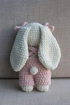 a knitted stuffed animal sitting on top of a couch next to a gray wall