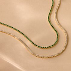 Luck is certain to find you while wearing our Emerald Tennis Choker Necklace. The vivid and brilliant color of the Emerald gemstone is perfect for a statement piece worn alone or to pair with other layering necklaces for a more boho, casual look. No matter which option you choose, you are sure to stand out. Finish/Material: 18K Gold Over Brass ∙ Rhodium Over Brass Featuring ~2mm CZ Emerald Gemstones on an adjustable 14 inch to 16 inch Choker Necklace Part of our Diamond and Pavé Collection Model Gold Tennis Necklace With Gemstones As Gift, Gold Emerald Necklace For Everyday Wear, Tennis Choker Necklace, Initial Tag Necklace, Dainty Initial Necklace, Diamond Tennis Necklace, Layering Necklaces, Tennis Necklace, Layered Jewelry