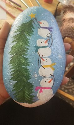 someone is holding an egg decorated with snowmen and pine trees on the side,