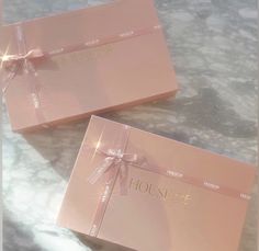 two pink boxes with bows on them sitting on a marble counter top next to each other