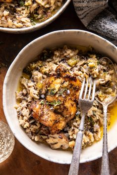 two bowls filled with chicken and rice on top of a wooden table next to silverware