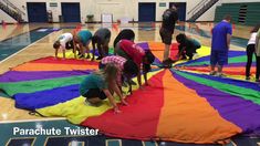 group of people standing on top of a multicolored parachute in an indoor gym