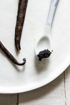 a spoon with some black stuff in it on a white plate next to two sticks