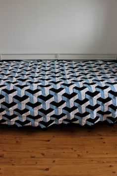 a bed with a blue and white bedspread sitting on top of a hard wood floor