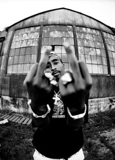 a black and white photo of a man making the v sign with his hands in front of a building