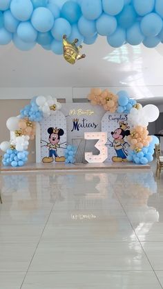 the balloon arch is decorated with mickey mouse balloons and blue streamers, along with an air - filled number