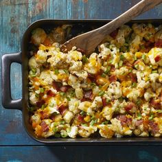 a casserole dish with bacon, cheese and green onions in it next to a wooden spoon