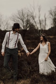 a man and woman holding hands in the grass with trees in the backgroud