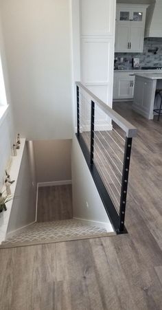 an empty room with wood flooring and white painted walls, stairs leading up to the kitchen