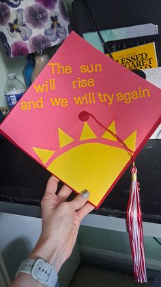 a person holding up a graduation cap that says the sun will rise and we will try again