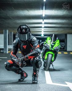 a man kneeling down next to a motorcycle in a parking garage with another motorcyclist behind him