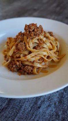 a white plate topped with pasta covered in meat and sauce on top of a wooden table