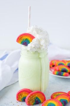 a jar filled with marshmallows and topped with whipped cream next to rainbow cookies