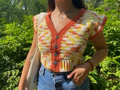 a woman standing in front of some bushes wearing a crochet top and jeans