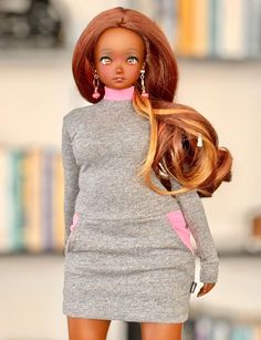 a barbie doll with long hair wearing a gray dress and pink heels in front of a bookshelf