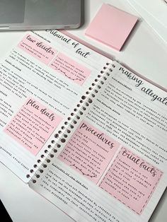 a notebook with pink sticky notes on top of it next to a laptop and pen