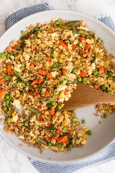 a white plate topped with fried rice and veggies next to a wooden spoon