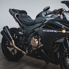 a black motorcycle parked in a room next to a white wall and wood flooring