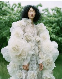 a woman with black hair wearing a white dress and flowers on her shoulders, standing in the grass