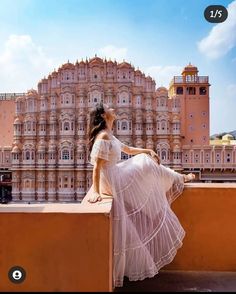 a woman sitting on top of a wall next to a tall building with a clock tower in the background