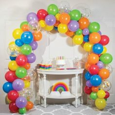 a rainbow themed birthday party with balloons and streamers on the arch, cake table