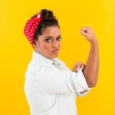 a woman in white shirt and red polka dot headband flexing her arm with both hands