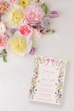 a bouquet of flowers next to a wedding card on a white surface with pink, yellow and purple flowers