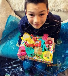 a young boy sitting on top of a blue plastic bag filled with lots of toys