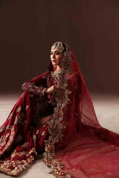 a woman in a red bridal gown sitting on the floor with her arms crossed