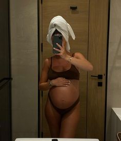 a pregnant woman taking a selfie in front of a mirror with her cell phone