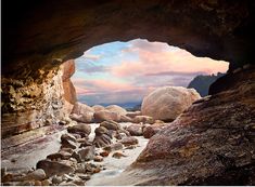 a cave entrance with rocks and water in the foreground at sunset or dawn, as seen from inside