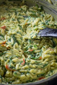 a pot filled with pasta and spinach on top of a stovetop next to a wooden spoon