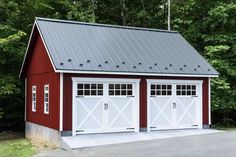 a red and white garage with two doors on the side, surrounded by green trees