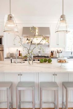 a white kitchen with four stools in front of the island and three lights hanging from the ceiling