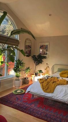 a bedroom with a large bed and lots of plants in the window sill next to it