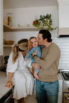 a man and woman holding a baby in the kitchen while they are kissing each other