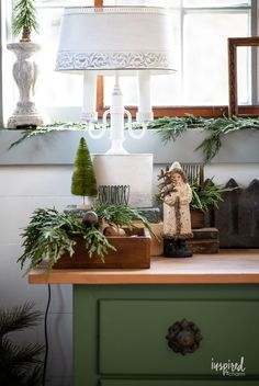 a green dresser topped with lots of christmas decorations and greenery next to a lamp