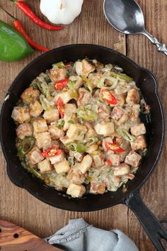 a skillet filled with food on top of a wooden table next to some spoons