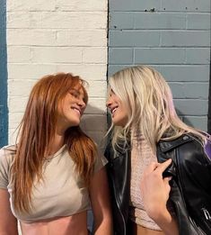 two beautiful women standing next to each other in front of a brick wall and blue door